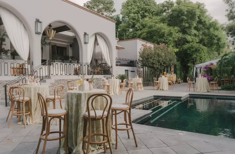 Recepción de coctel junto a la alberca con mesas altas y área lounge