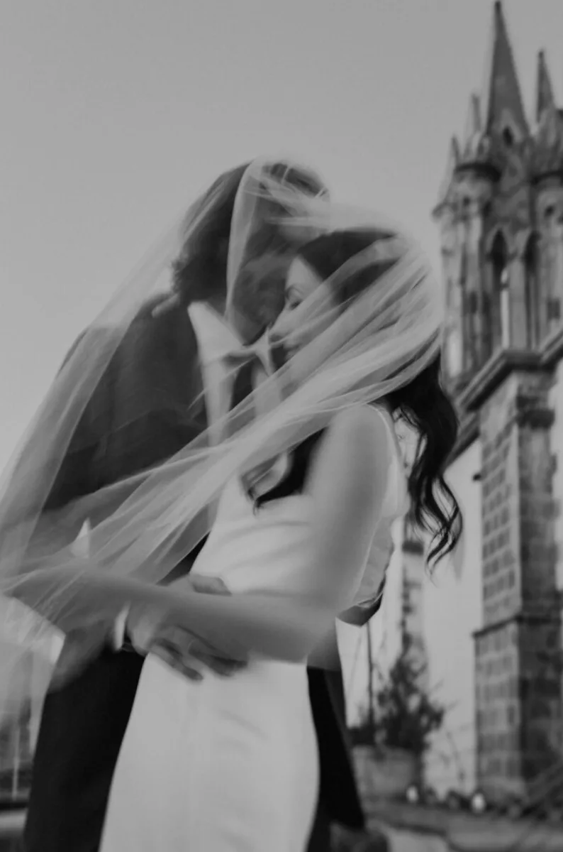 Retrato editorial en blanco y negro de recién casados bajo un velo en movimiento en San Miguel de Allende
