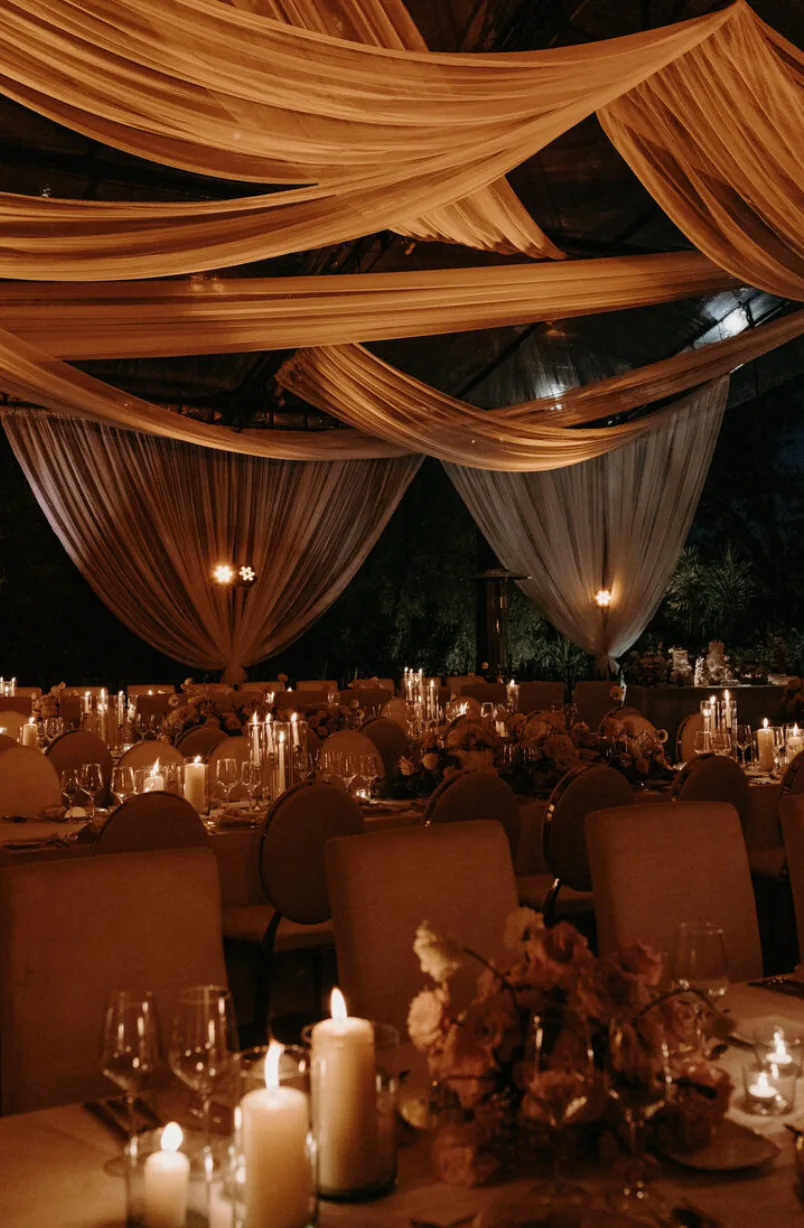 Recepción de boda iluminada con velas y telas suspendidas