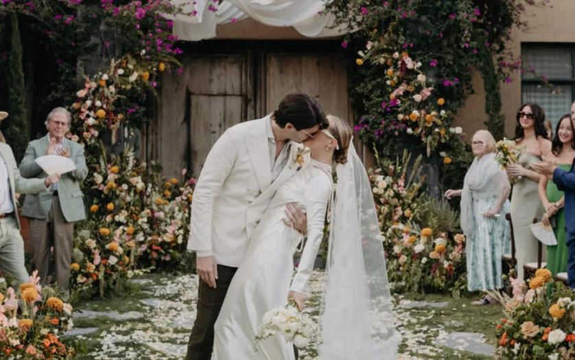 Recién casados besándose bajo un colorido arco floral en el jardín