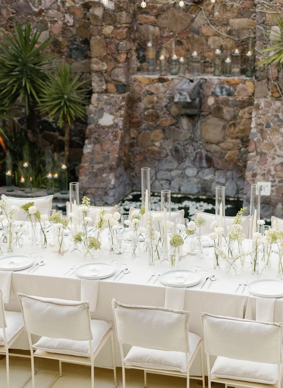 Elegante mesa de recepción en blanco junto a una fuente de piedra y velas flotantes