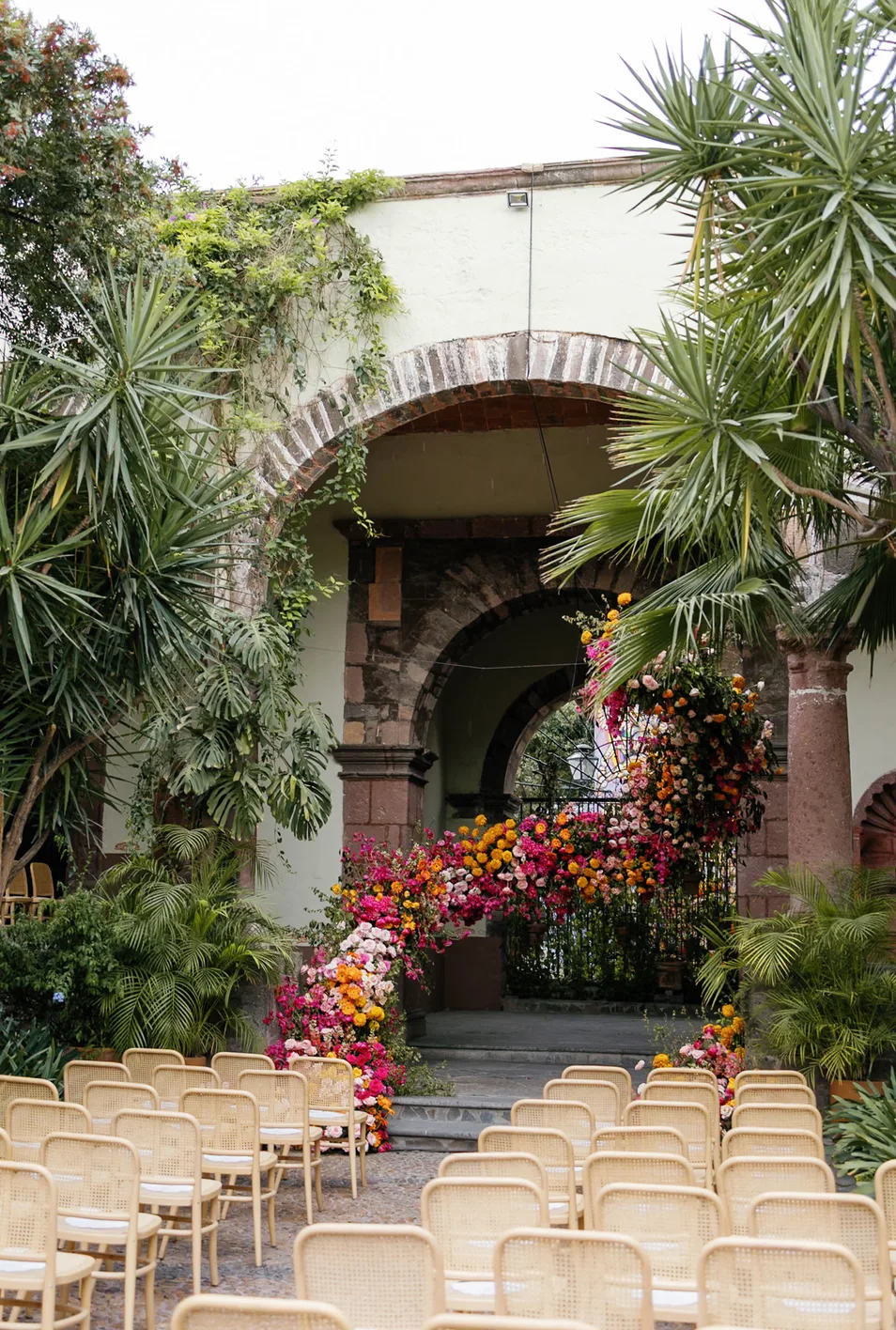 Pasillo de boda en patio que conduce a un vibrante arco floral asimétrico