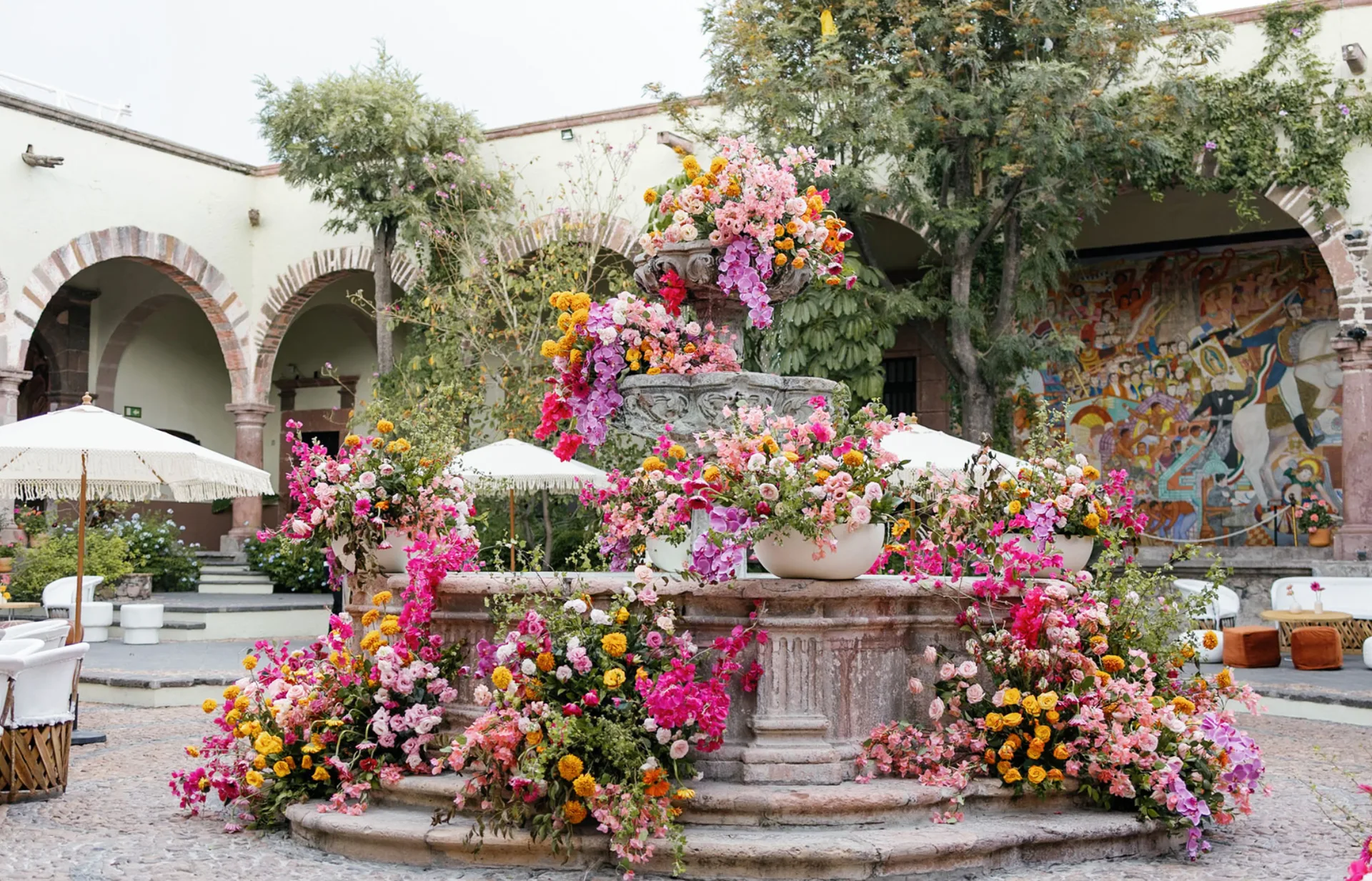 Fuente de patio histórico cubierta con vibrantes flores rosas, naranjas y amarillas para una boda