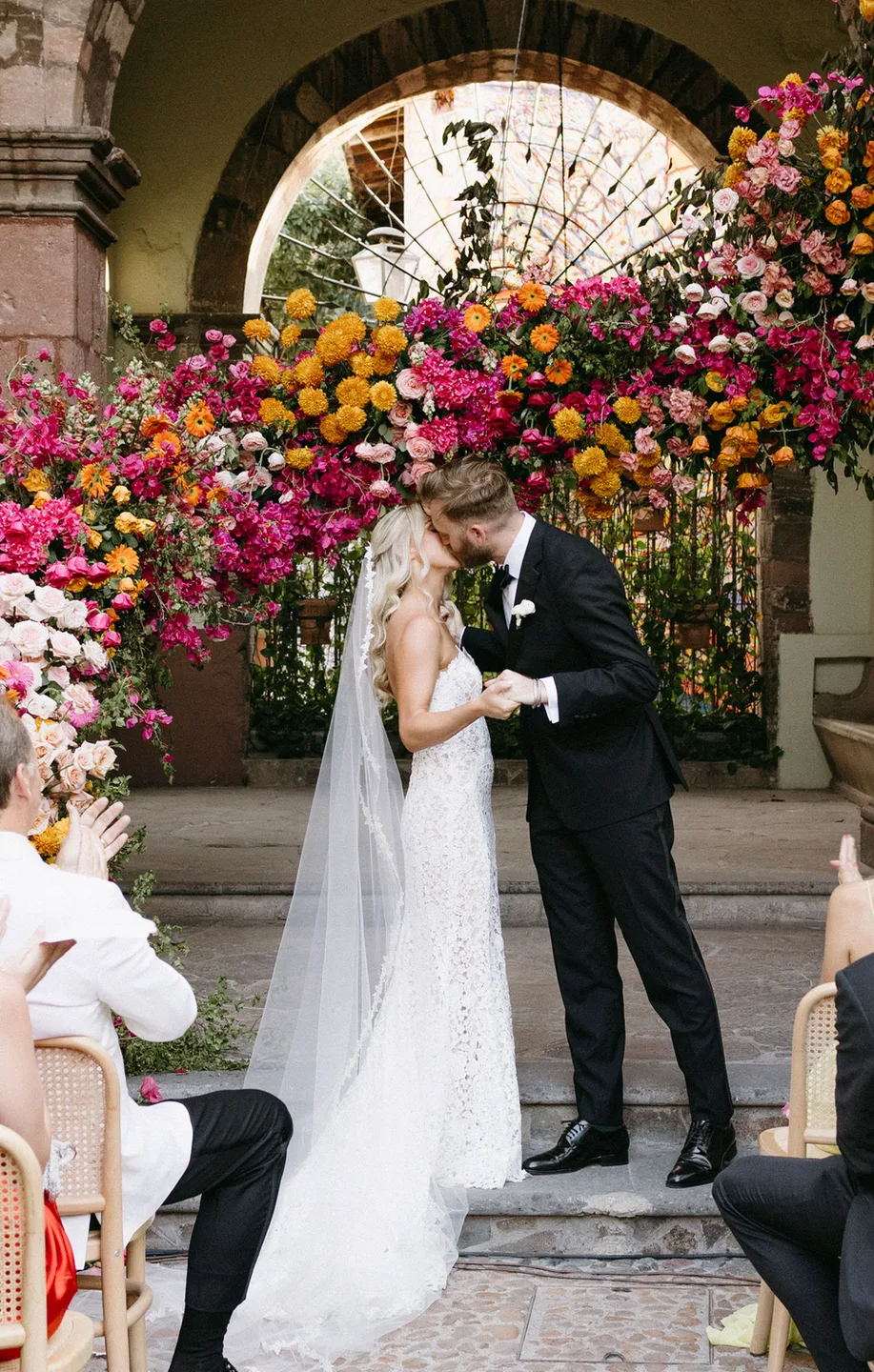 Recién casados besándose bajo una espectacular instalación floral colorida para ceremonia