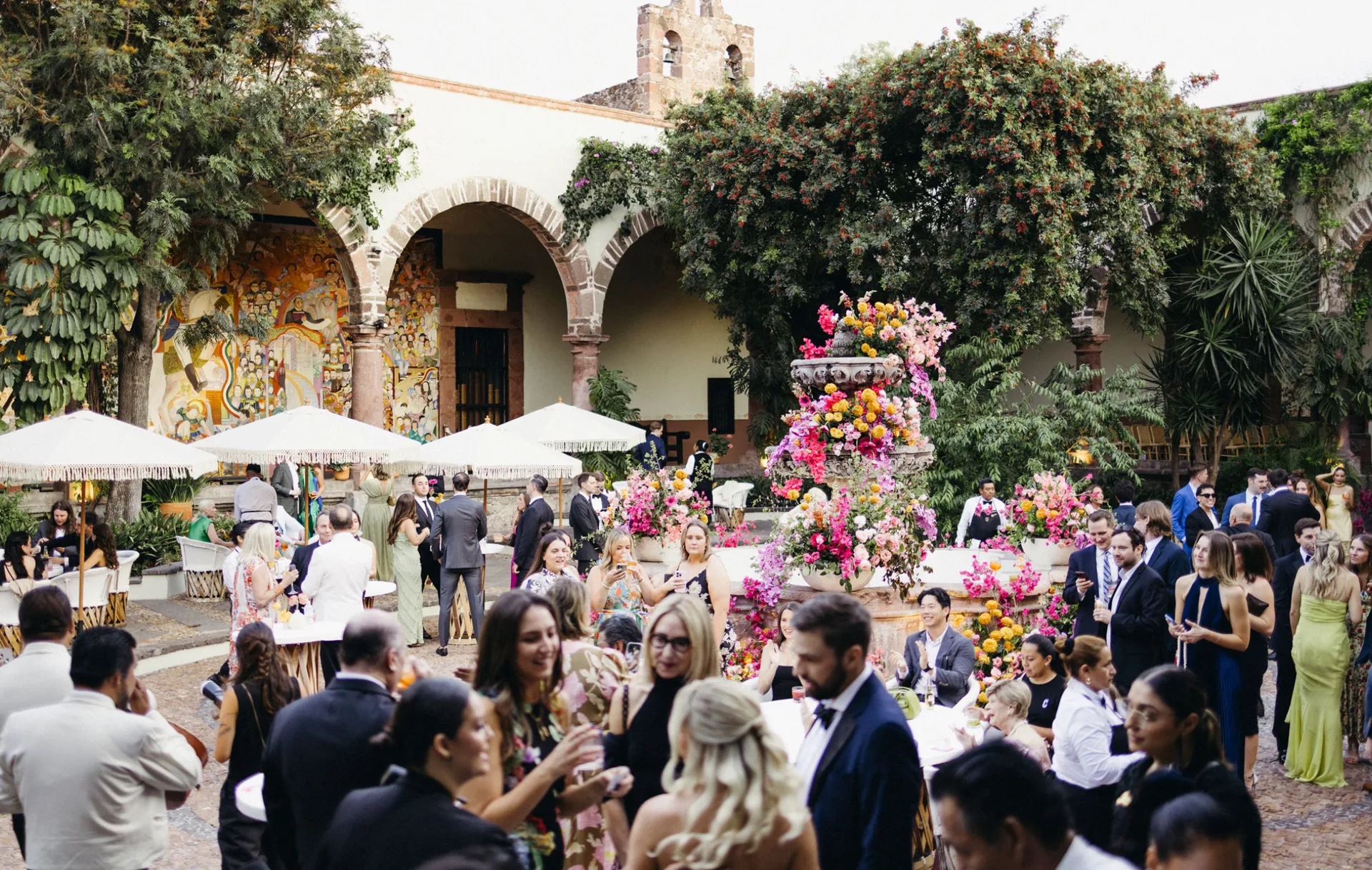 Invitados reunidos alrededor de una fuente cubierta de flores durante un coctel en patio