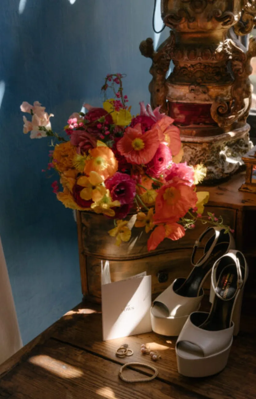 Zapatos de novia, joyería y un ramo vibrante dispuestos en un interior histórico