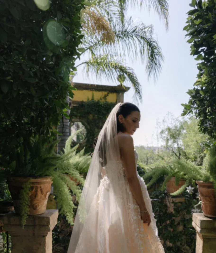 Novia con vestido de encaje y velo posando en un jardín exuberante