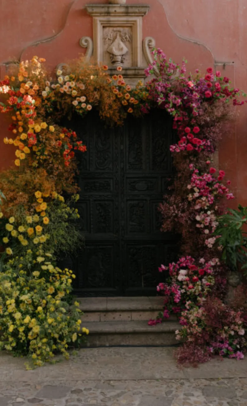 Puerta colonial enmarcada por una abundante instalación floral multicolor