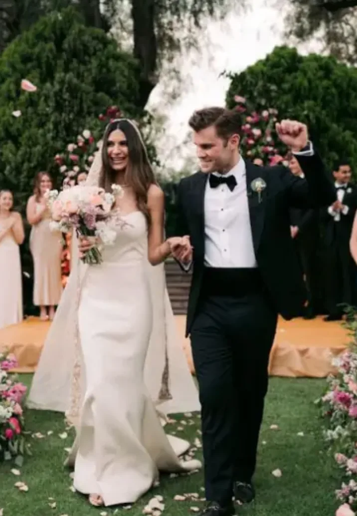 Recién casados celebrando al salir de una ceremonia en jardín enmarcada con flores