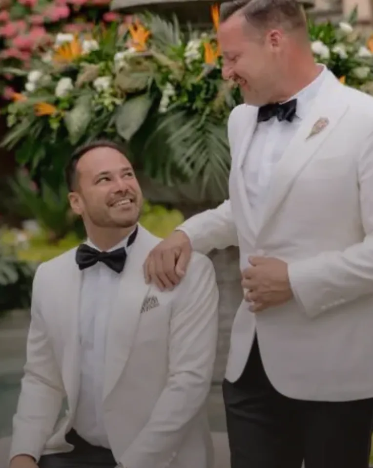 Dos novios sonriendo frente a una instalación floral tropical para ceremonia