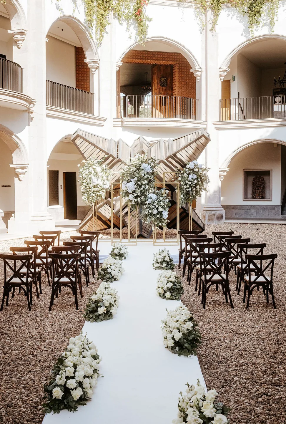 Pasillo de ceremonia con flores blancas en un luminoso patio de arcos