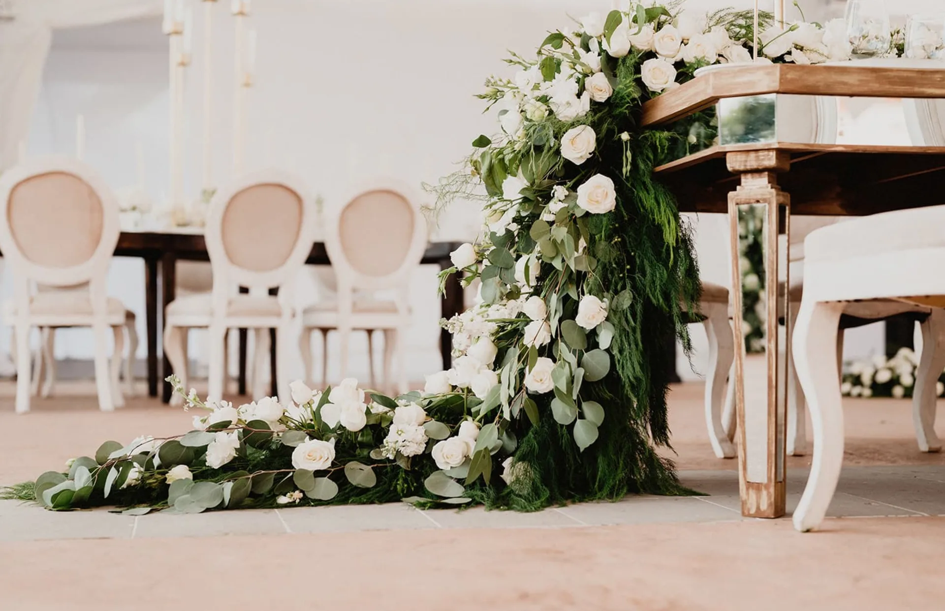 Rosas blancas y follaje en cascada decorando una mesa de boda con espejo