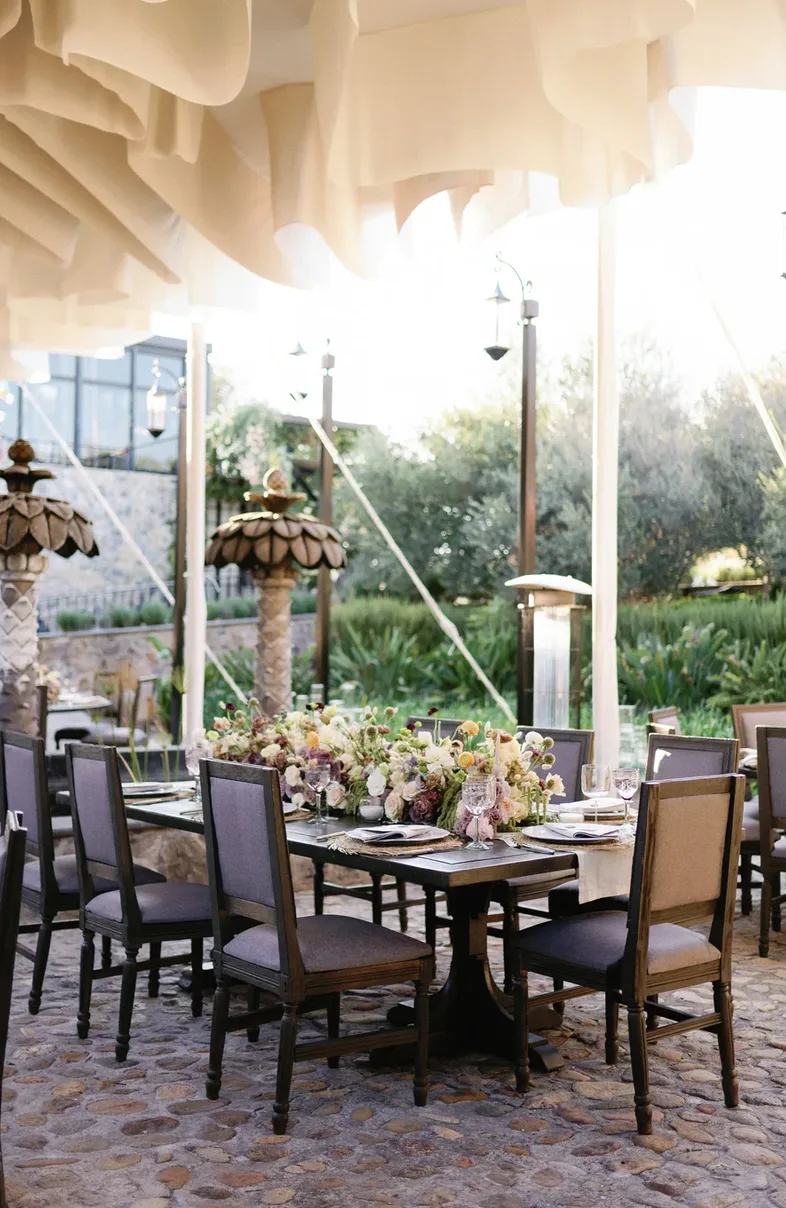 Mesas de recepción con flores bajo un dosel de tela en la terraza del jardín